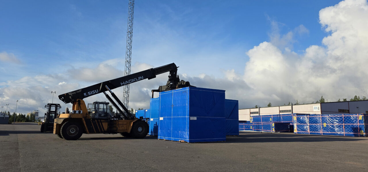 Reach stacker moving blue-wrapped industrial cargo in a port storage area as part of a large-scale project logistics operation.