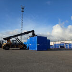 Reach stacker moving blue-wrapped industrial cargo in a port storage area as part of a large-scale project logistics operation.